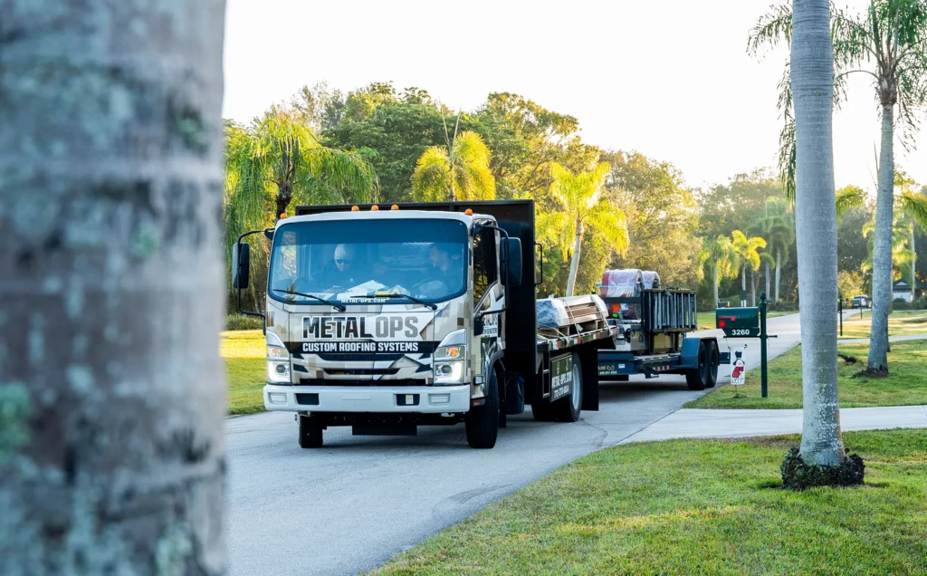 A truck labeled "Metal Ops Custom Roofing Systems" is parked on a suburban street with palm trees, carrying roofing materials and towing a trailer in the background.
